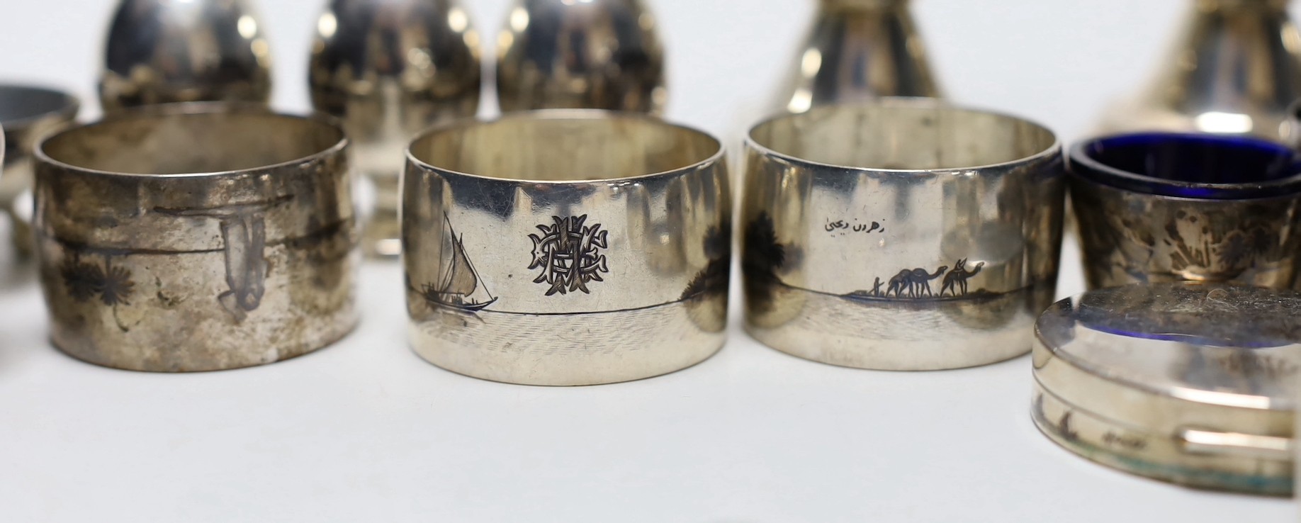 Thirteen assorted Iraq white metal and niello condiments, circular box, five similar napkin rings, a brooch and a pair of similar (damaged) candlesticks.